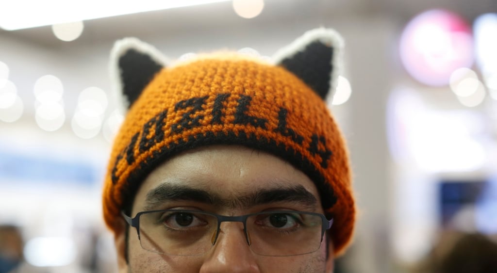 tanned man, glasses, orange hat with black years, mozilla written in black, glasses,