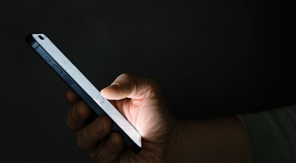 white phone screen held inright hand, shown from profile, dark room