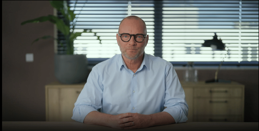 soren odido, white shirt, hands on table, bald man, no tie, black glasses frames, plant
