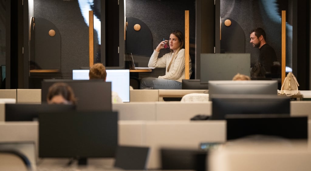 three soundproof office pods, young woman in middle, red smartphone