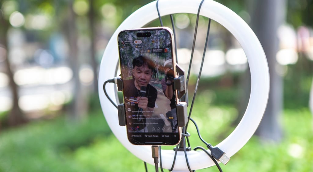 indonesian man on smartphone screen, wires, green grass, circular lamp, tiktok live stream