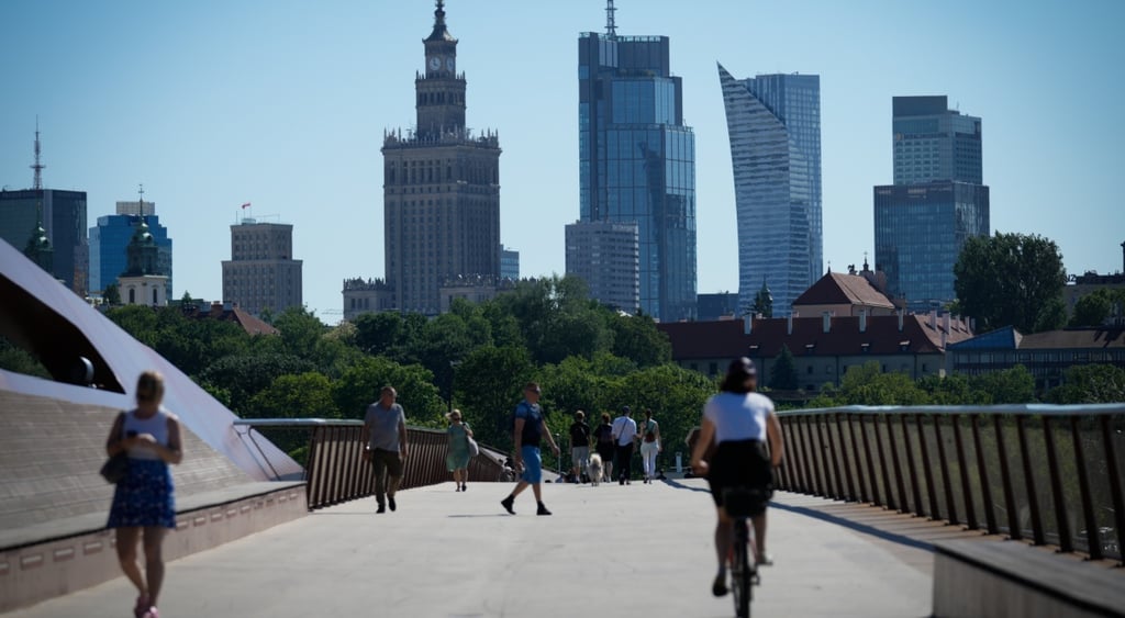 five tall glass buildings, clear blue sky, pedestrian bridge, people, bike