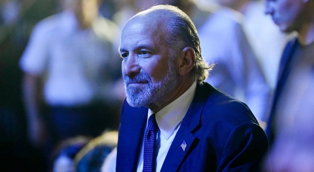 Howard Lutnick in blue light, bald forehead, grey beard and moustache
