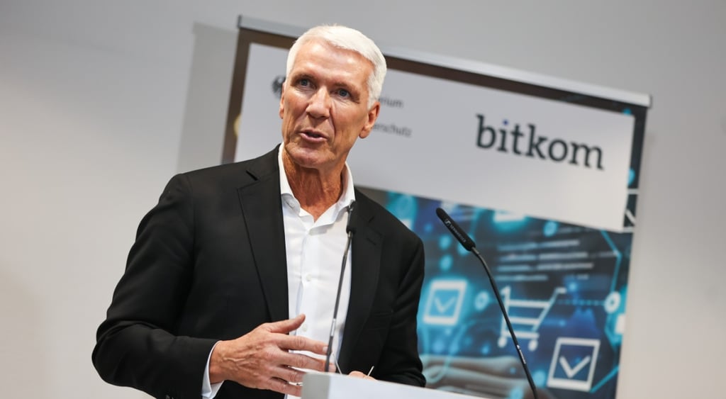 white man, black jacket, white collar shirt, no tie, white hair, bitcom poster, white wall