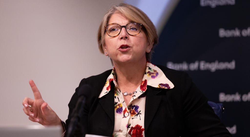 Sarah Breeden, black blazer, white collar shirt with dark red flowers, blonde hair, glasses