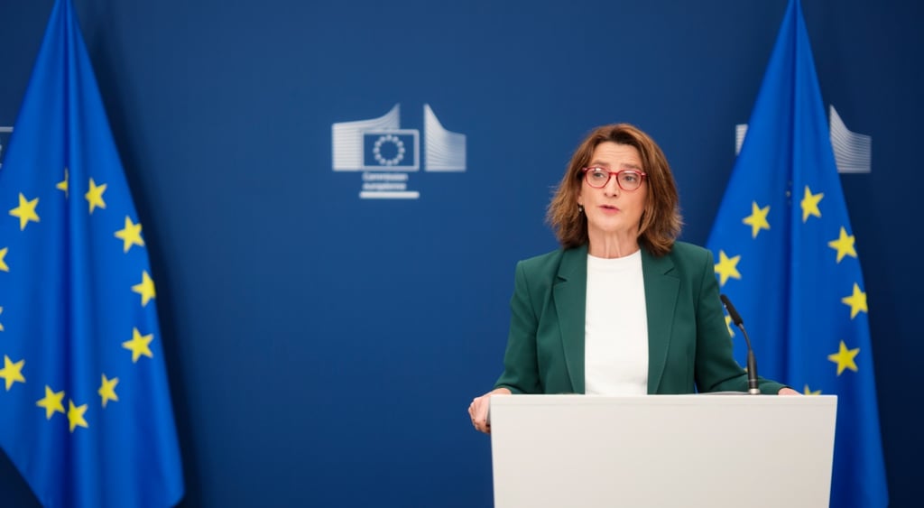 Teresa Ribera, dark green jacket, white blouse, two EU flags, dark blue photo wall, white podium