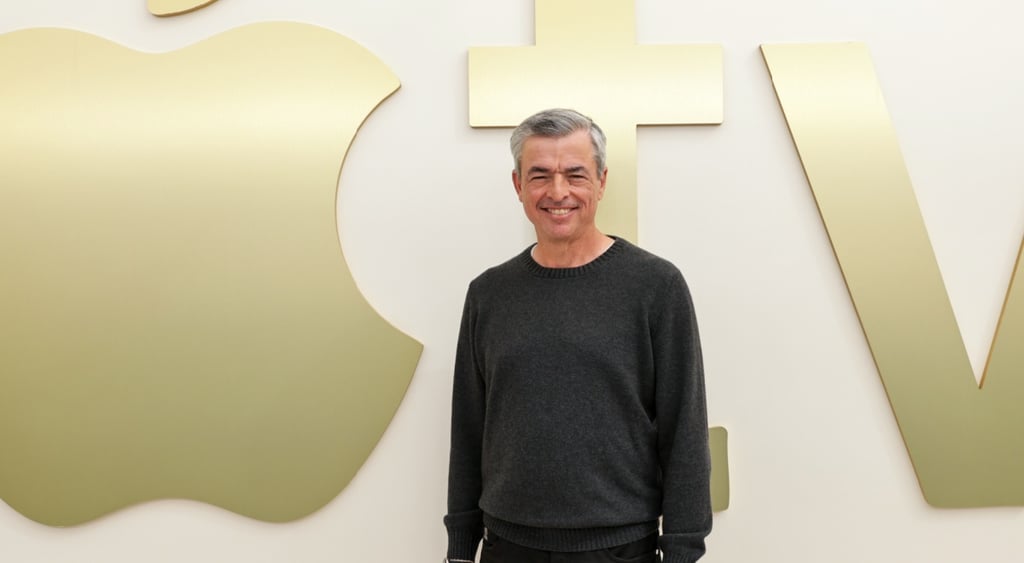 Eddy Cue, over fifty year old white male, grey hair, black long sleeve top, smiling, golden apple