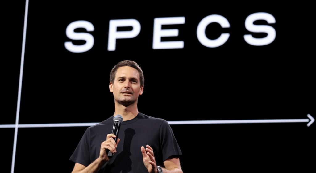 Evan Spiegel, young white male, microphone in hand, black t-shirt, black backgrous, specs in white