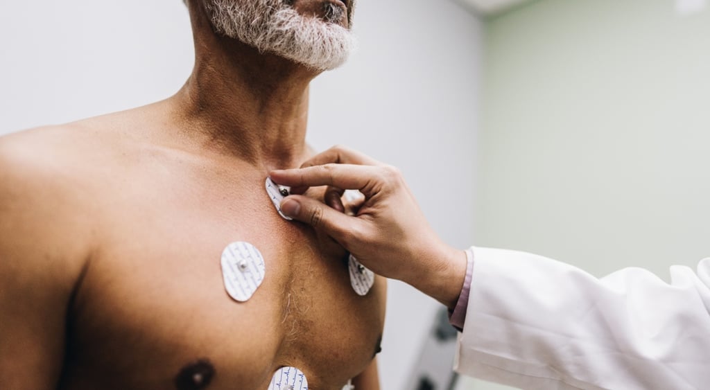 white doctor hand, white scrub sleeve, white round sensors on brown man chest, grey beard
