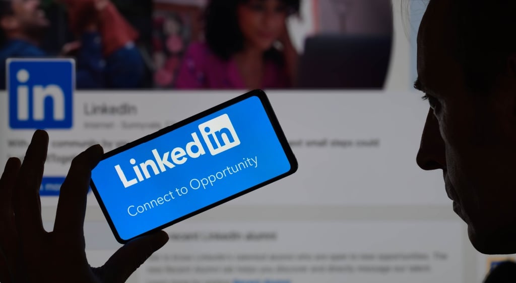 linkedin logo on smartphone screen, open profile page in the background, man face in the shadow