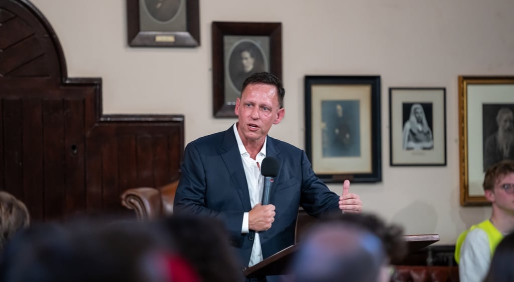 peter Thiel, dark suit ,white collar shirt, no tie, five painting, black mic, people, lack hair,
