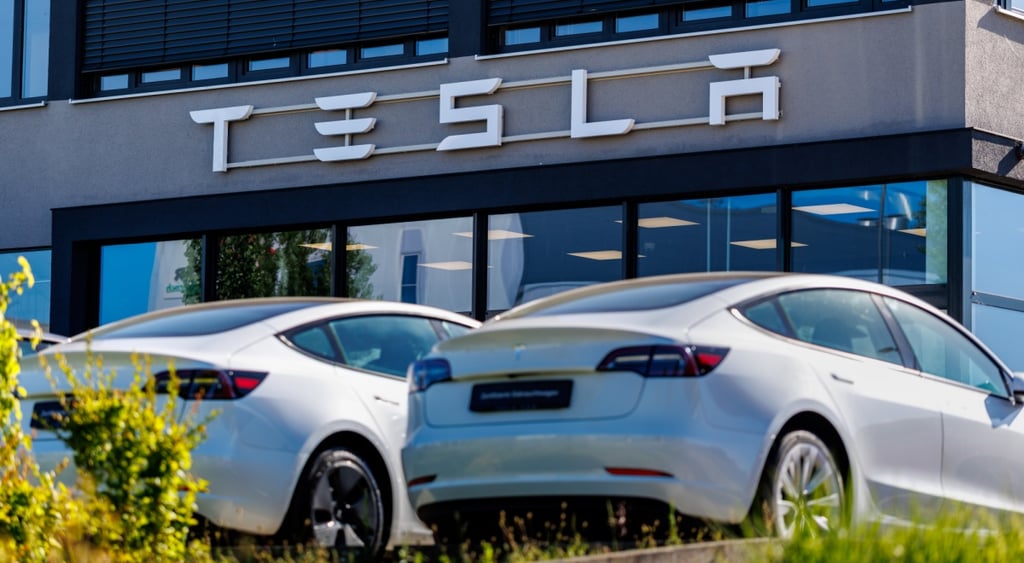 two silver resla cars, tesla building, glass wall, green grass, blue reflected sky in glass wall