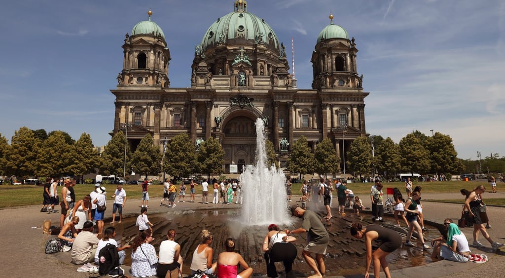 old building, light green round roof, round fountain, water, people sitting around, summer, white, red shirts, shorts