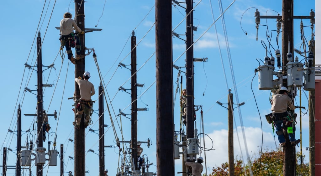 tlls power line polls, men tied to them fixing boxes, blue sky, some white clouds