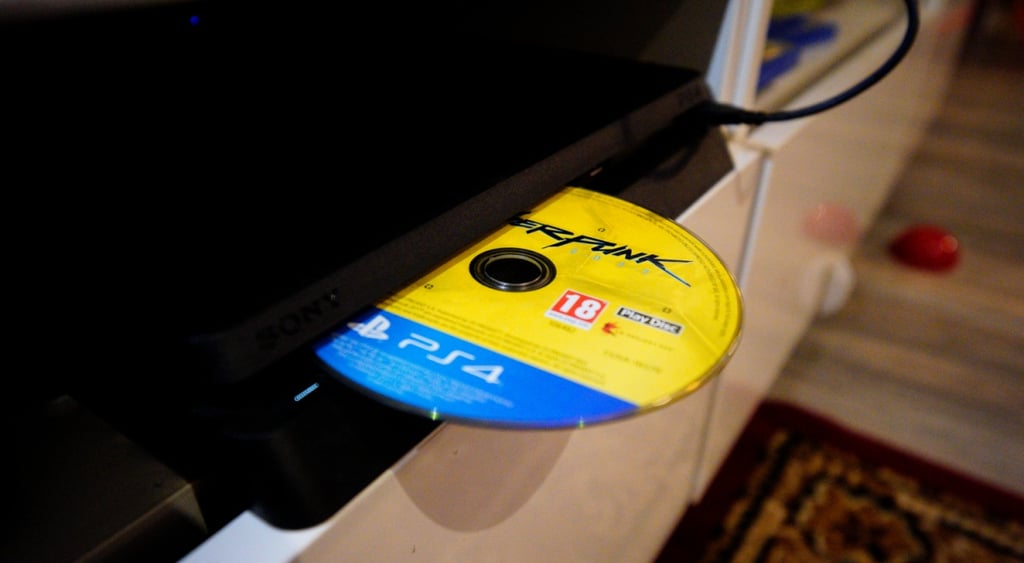 ps4 black console, yellow and light blue disc, light wood floor, ornamented carpet