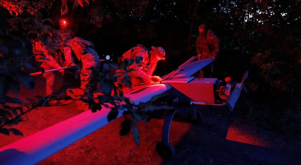 four ukrianian soldiers prepare huge drone in dark surrounded by trees in red light