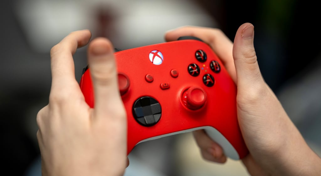 white child's hands are holding a red xbox controller, black and red buttons, white xbox logo