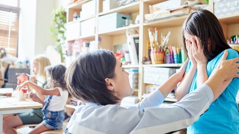 Side view of young female teacher comforting crying girl during lesson