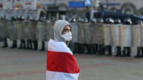 An opposition supporter wearing a protective face mask holds a historical white-red-white flag of Be