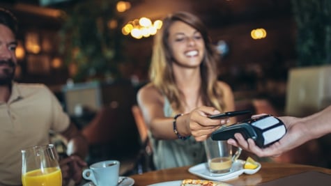 Happy couple using mobile phone and making contactless payment in a restaurant