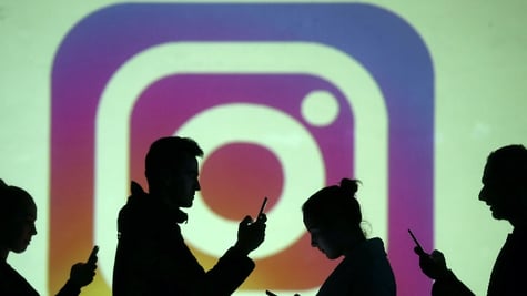 Silhouettes of mobile users are seen next to a screen projection of the Instagram logo