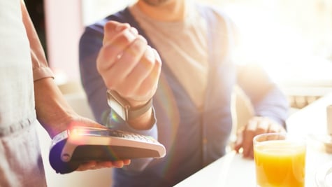 Hand of businessman with smartwatch over payment machine held by waitress