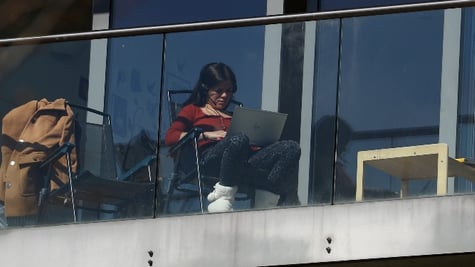 A woman looks at her laptop on a balcony of an apartment block
