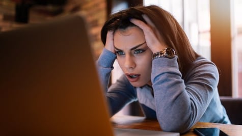 Woman with hands over head looking at PC screen