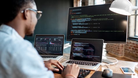 Coder in front of three computers with code on screens