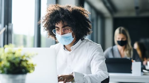 Person with mask sitting in front of PC