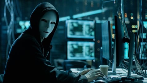 Hacker with white mask in a blue room full of computers