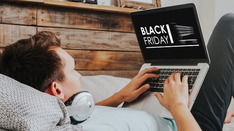 Young man laying on bed and looking at laptop screen with Black Friday