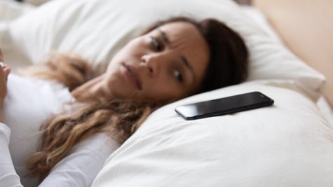 Woman laying on bed and looking anxiously at mobile nearby