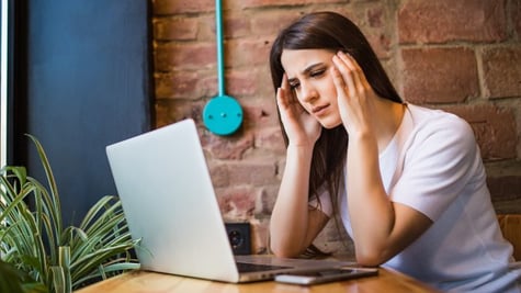 Concerned woman holding hands on head and looking at PC