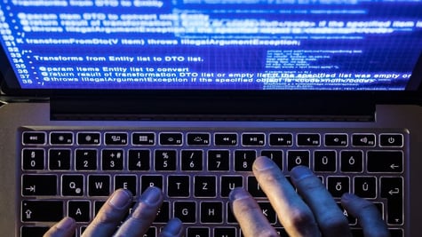 fingers typing on laptop keyboard and blue screen with many inscriptions
