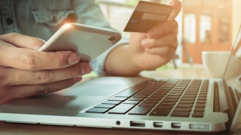 Man holding mobile and credit card above laptop