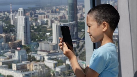 A Muslim boy uses a smarphone against the background of a panoramic window. Blurred view of the city