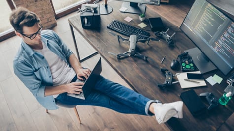 High angle view of a focused man typing laptop with legs on table