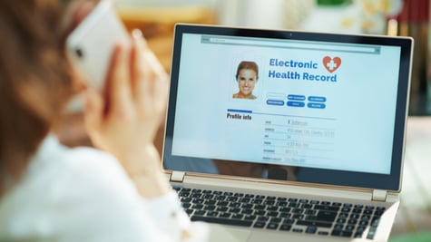 Seen from behind woman at home in sunny day using a cell phone and checking electronic health record