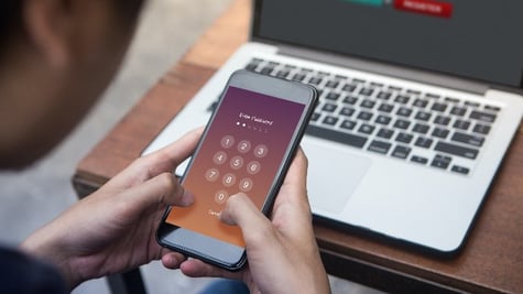 Businessman working on laptop and trying to enter password on his smartphone at outdoor cafe