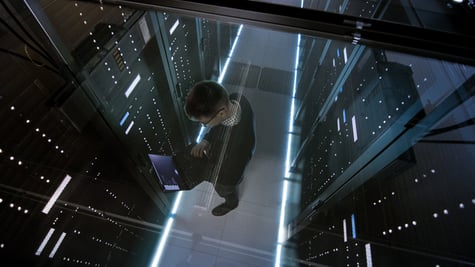 Top View Through the Glass of IT Engineer Working with Laptop in Data Center Full of Active Rack Ser