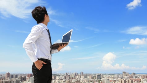 Young business man using laptop and looking at blue sky