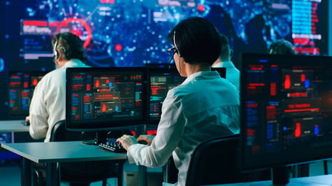 Rack focus of anonymous men and woman sitting at desk and writing security codes on computers during