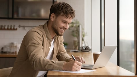 Close up smiling young man using laptop, writing, taking notes, watching webinar, training, involved