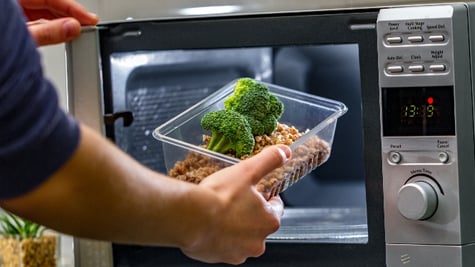 Using the microwave oven to heat food. Woman's hand puts plastic container with broccoli and buckwhe