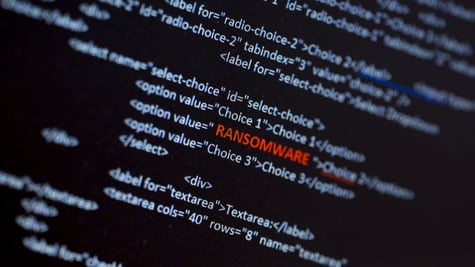 Ransomware text in red in the middle of the computer screen surrounded by computer code language