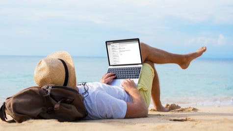 Man reading email on laptop while relaxing on beach