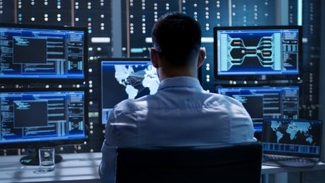 Man in blue light background working with multiple computers