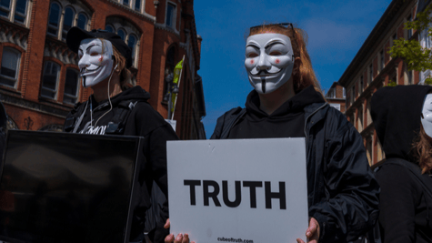 Three protesters wearing V masks on the street with a sign saying TRUTH