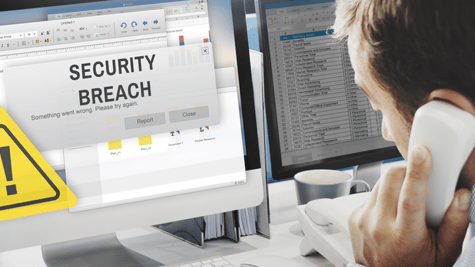 Man on phone as DATA BREACH warning flashes on his computer screen